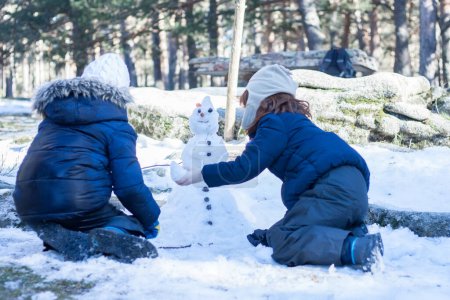 Foto de Dos hermanos haciendo un muñeco de nieve en la montaña nevada. Colaboración. día de invierno Horizontal. Vista trasera - Imagen libre de derechos