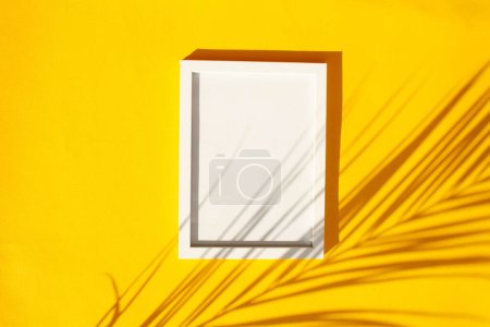 Téléchargez les photos : Cadre blanc vide avec ombre contrastée de feuille de palmier sur fond jaune. Style de pose plat - en image libre de droit