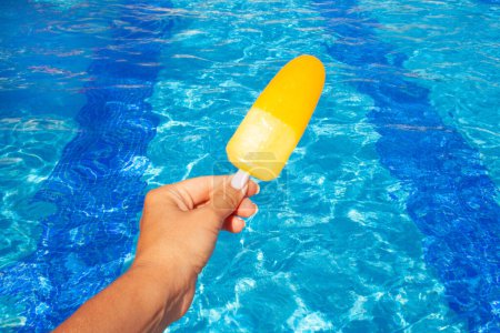 Photo for Hand holds yellow ice cream on the background of the pool. Summer concept, vacation - Royalty Free Image
