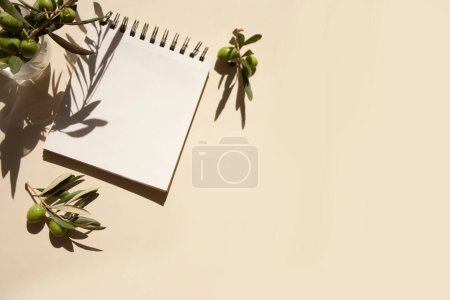 Foto de Mockup cuaderno vacío para escribir y ramitas de olivo en una vista superior de mesa beige. Estilo de moda contrastando sombras - Imagen libre de derechos