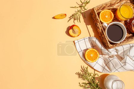 Foto de Desayuno soleado por la mañana. Café, zumo de naranja, frutas frescas en una canasta de mimbre sobre un fondo de melocotón. Estilo de laico plano - Imagen libre de derechos