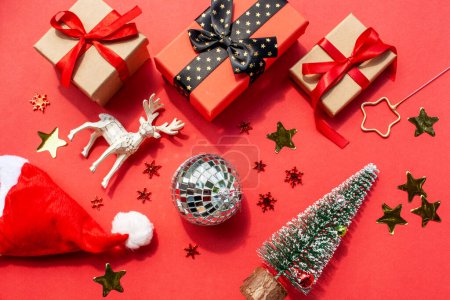 Foto de Banner de año nuevo con sombrero de santa, ciervos navideños y cajas de regalo sobre fondo rojo. Estilo laico plano - Imagen libre de derechos