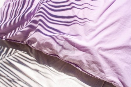 Téléchargez les photos : Linge blanc et oreillers lavande. Textiles naturels. Tendance ombres contrastées avec des feuilles de palmier - en image libre de droit