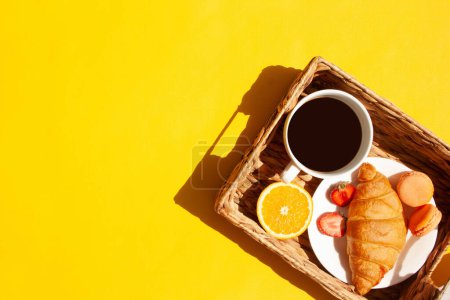 Téléchargez les photos : Panier en osier avec une tasse de café, croissant, macaron et fruits. Petit déjeuner matinal - en image libre de droit