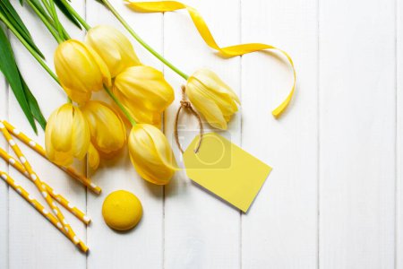 Photo for Yellow tulips, tubules and macarons on a white wooden background. Flat lay style. Spring time - Royalty Free Image