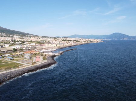 Téléchargez les photos : Une vue aérienne capturant le contraste à couper le souffle entre la mer bleu profond et la zone urbaine densément peuplée de Granetello à Portici, avec des montagnes offrant une toile de fond pittoresque - en image libre de droit