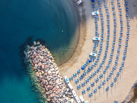 An aerial view of Palinuros beach with neatly arranged blue umbrellas a rocky outcrop and clear blue green waters