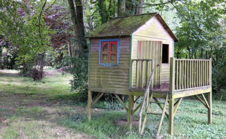 Téléchargez les photos : Une vieille maison de jeux avec une véranda dans une forêt. Une petite maison en bois devenue verte au fil des ans. Fond vert naturel et espace de copie. - en image libre de droit