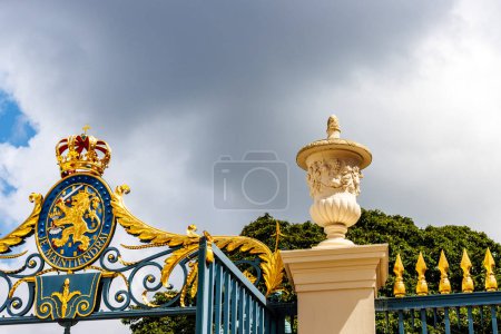 Goldenes Wappen der niederländischen Königsfamilie am Zaun des Palastes Noordeinde vor dunklen Wolken, Den Haag, Niederlande, Europa