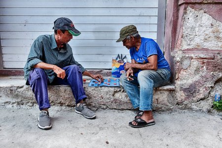Photo for HAVANA, CUBA - JANUARY 1, 2020:  Two unidentified men play a game of checkers on the sidewalks of Havana whil sitting on a door step. - Royalty Free Image