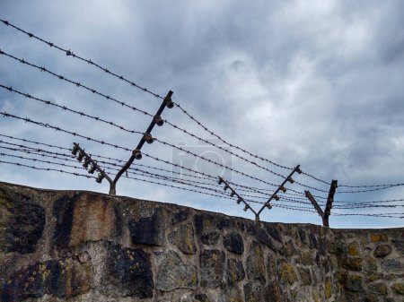 Photo for MAUTHAUSEN, AUSTRIA - DECEMBER 4, 2022: A stark view of a barbed wire fence on top of one of the stone walls at the Mauthausen concentration camp in Austria. - Royalty Free Image