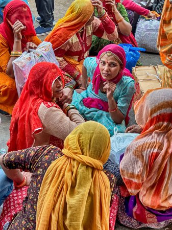 Foto de JODHPUR, INDIA - DECEMBER 30, 2022: A group of unidentified woman in colorful clothing sit on the street after shopping in the Jodhpur market and wait for something to happen. - Imagen libre de derechos