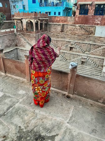 Foto de JODHPUR, INDIA - DECEMBER 31, 2022: An unidentified woman stands at the edge of the Toorji Ka Jhalra Bavdi step well in Jodhpur in order to feed the fishes with bread crumbs. - Imagen libre de derechos
