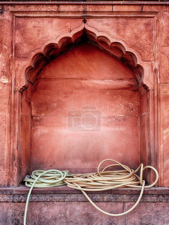 Foto de Las mangueras de agua amarilla se enrollan libremente en un nicho de pared en la mezquita Jama Masjid en Delhi, India. - Imagen libre de derechos