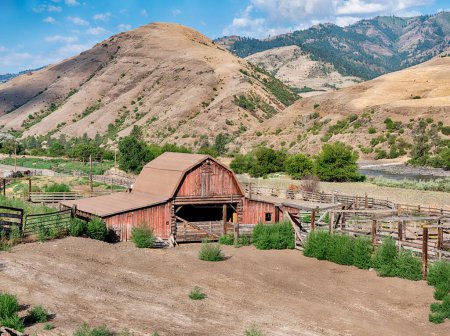 Téléchargez les photos : Un ranch rural près de Lucile, Idaho comprend une grange rouge classique et un corral de bois à côté de la rivière Lower Salmon et des montagnes.. - en image libre de droit