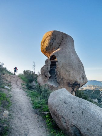 Foto de Un caminante anónimo cruza la cima de una colina en el desierto de Baja California cerca de Tecate con una enorme roca junto al sendero. - Imagen libre de derechos