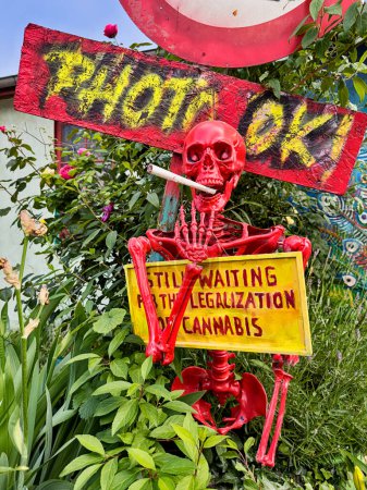 Téléchargez les photos : COPENHAGUE, DANEMARK - 15 JUIN 2023 : Un panneau de protestation plaidant pour la légalisation du cannabis est tenu par un squelette rouge avec un joint géant dans la communauté Chrisitiana Freetown à Copenhague, Danemark. - en image libre de droit