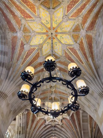 Foto de Una lámpara de araña proporciona iluminación en un pasillo gótico con un techo de piedra decorativa. - Imagen libre de derechos
