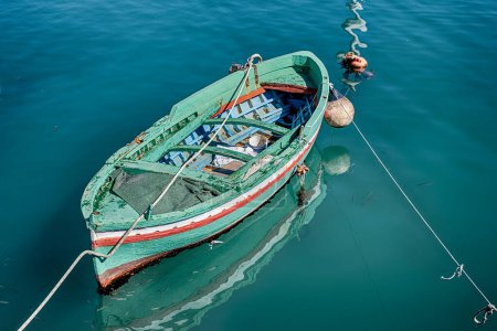 A green wooden boat is moored in one of the small stone harbors in the city of Siricusa, Italy.