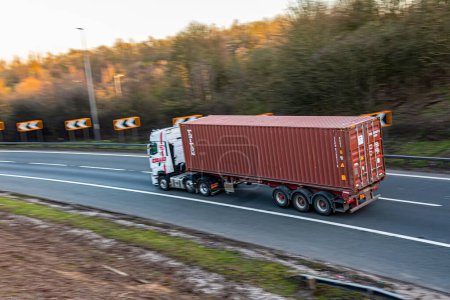 Téléchargez les photos : Watford, Royaume-Uni - 4 avril 2023 : Camion avec conteneur d'expédition brun en mouvement sur l'autoroute britannique M1 - en image libre de droit