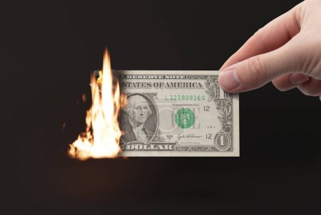 Hand holds a burning dollar bill. The concept of destroying money, spending money, losing money.