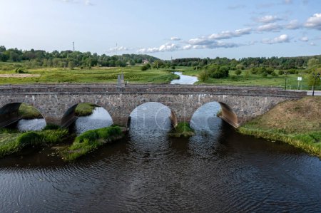 Photo for Stone bridge spanning river in grassy field.Kandava, Latvia - Royalty Free Image