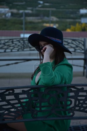 Téléchargez les photos : Jeune femme en chapeau et robe noire sur un banc dans le parc - en image libre de droit