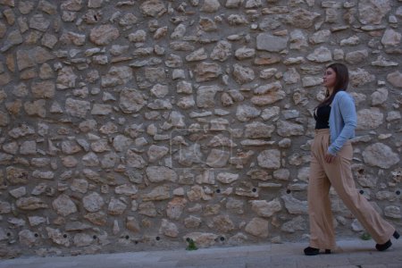 Téléchargez les photos : Jeune femme en robe blanche avec un sac à dos sur le fond du vieux mur de pierre - en image libre de droit