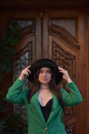 Téléchargez les photos : Belle jeune femme dans un chapeau et manteau noir posant sur un fond de maison en bois - en image libre de droit