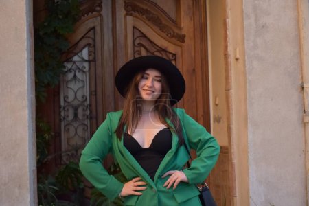 schöne junge Frau mit Hut und schwarzem Kleid posiert auf der Straße