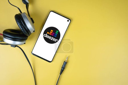 Photo for Deezer app logo on smartphone screen and headphones with jack on yellow background with copy space, top view. Swansea, UK - November 1, 2022 - Royalty Free Image