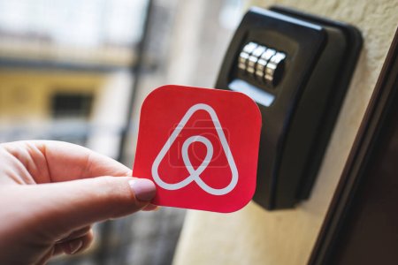 Foto de Airbnb logo next to a smart key lock box. Contactless check-in to the holiday apartment, short term accommodation bookings for tourists. Budapest, Hungary - February 3, 2023. - Imagen libre de derechos