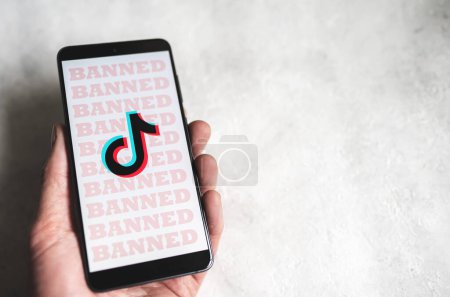 Téléchargez les photos : TikTok app logo with Banned sign on phone screen in hand. Tik Tok ban in the US for the security concerns concept. Concrete background with copy space. Swansea, UK - February 15, 2023. - en image libre de droit
