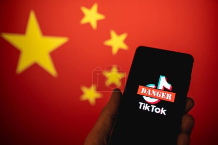 Téléchargez les photos : Logo de l'application TikTok rayé avec le signe Danger rouge affiché sur l'écran du téléphone avec le fond du drapeau de la Chine. TikTok est dangereux pour la vie privée et la sécurité concept. Swansea, Royaume-Uni - 21 février 2023. - en image libre de droit