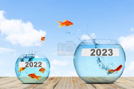 Téléchargez les photos : Image de poissons dorés sautant du petit aquarium avec des nombres 2022 au grand aquarium avec des nombres 2023 en fond bleu ciel - en image libre de droit