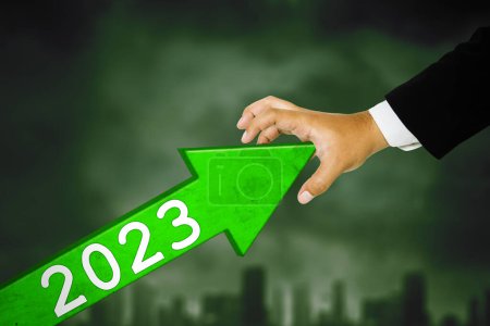 Photo for Close up of businessman hand try to hold back an upward arrow of 2023 number with cloudy sky background - Royalty Free Image