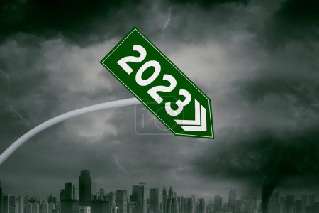 Foto de Primer plano de la flecha declinante en forma de letrero verde con número 2023 en el fondo de la ciudad tormentosa - Imagen libre de derechos