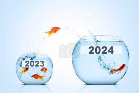Téléchargez les photos : Poisson doré bondissant d'un aquarium plus petit à un aquarium plus grand avec 2024 numéros de nouvelle année sur fond bleu - en image libre de droit