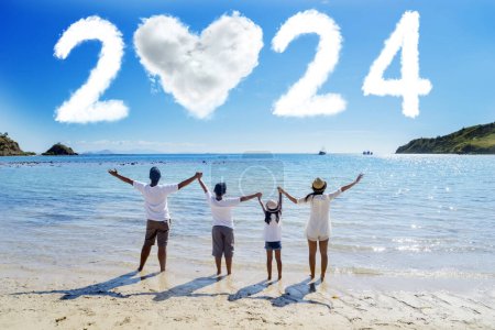 Foto de Familia alegre de pie juntos mirando los números en forma de nubes 2024 números de año nuevo y el corazón. Disparo en la playa - Imagen libre de derechos