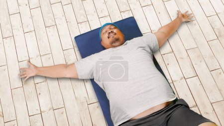 Téléchargez les photos : Vue du haut vers le bas de l'obésité homme portant des vêtements de sport tout en faisant s'asseoir sur le sol en bois - en image libre de droit
