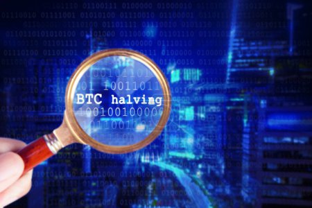 Bitcoin Halving 2024 - Hand holding a magnifier looking at BTC halving written on binary code
