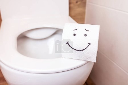 Primer plano de un rollo de papel higiénico con un emoji divertido colgando en la pared del baño. El concepto de buena salud, baño limpio, vida feliz. Copiar la pasta para su diseño y texto