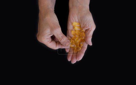 Photo for Close-up of an elderly womans hand with a handful of Omega 3 vitamins. Black background, copy paste for your text. The concept of health prevention, taking vitamins and minerals, maintaining the body - Royalty Free Image