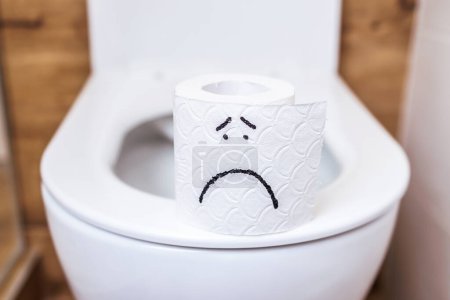 Photo for Close-up roll of white toilet paper with a painted sad face stands on the toilet. The concept of bad mood, health problems, constipation, hemorrhoids, intestinal problems. Personal hygiene, self care - Royalty Free Image