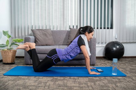 Photo for Woman in sportswear is sitting on a mat to do yoga exercise in the indoor living room at home on holiday cozy, relaxing and healthy concept. - Royalty Free Image