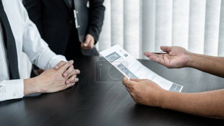 Businessman candidate present and explaining his profile to selection committee manager and recruiter reading a resume during a job interview in office.