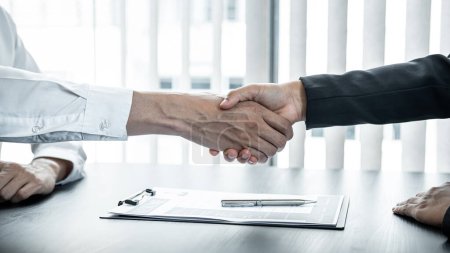 Man employer is shaking hands to congratulate the new employee after successful job interview and signing the contract in meeting room at office.