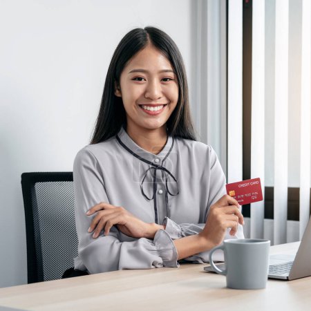 Photo for Asian woman holding credit card and using laptop for online shopping to purchasing product on website while smiling to looking at the camera and using credit card to paying money on internet banking - Royalty Free Image
