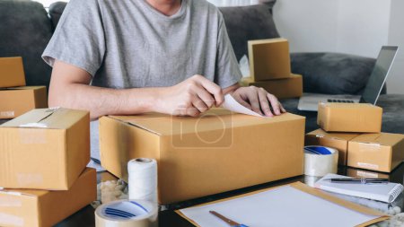 Photo for Young entrepreneur SME man receive order client and working with packaging sort box delivery online market on purchase order and preparing package product, Small business parcel for shipment. - Royalty Free Image