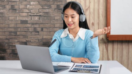 Photo for Female tutor wearing headset, using laptop and though camera to teaching new lesson by video conference on webcam while explaining math equations and physic formula on e-learning course for student - Royalty Free Image
